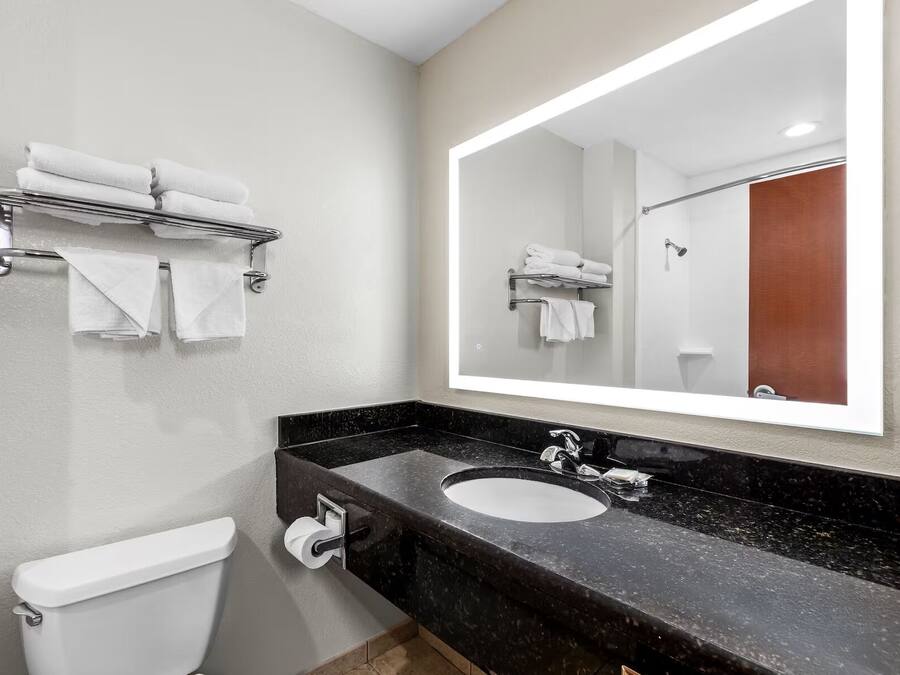 A modern bathroom with a black marble sink, a toilet, and a towel rack with folded towels.