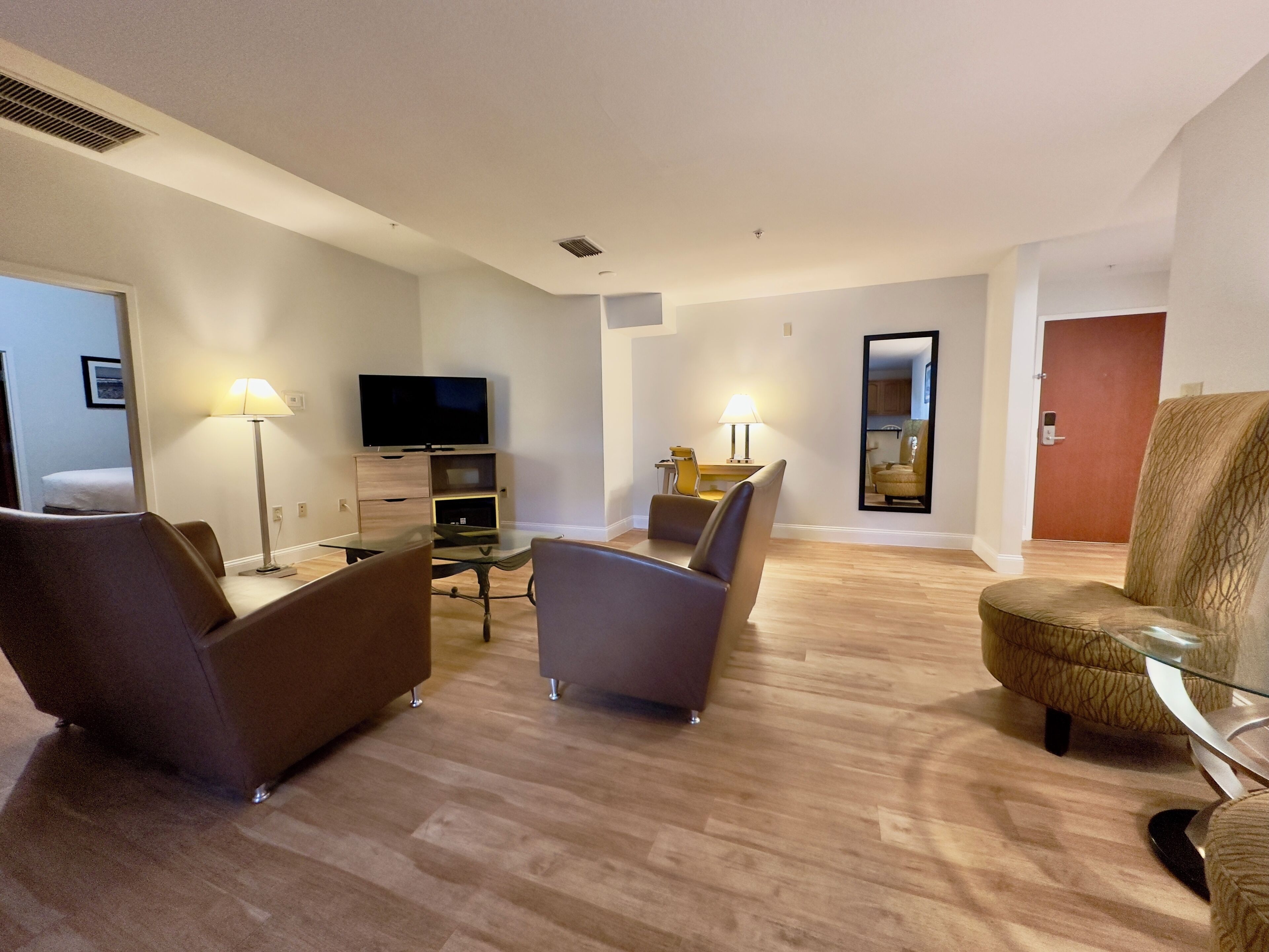 Una sala de estar moderna con un televisor de pantalla plana, dos sillones, una mesa de centro de vidrio y una lámpara.