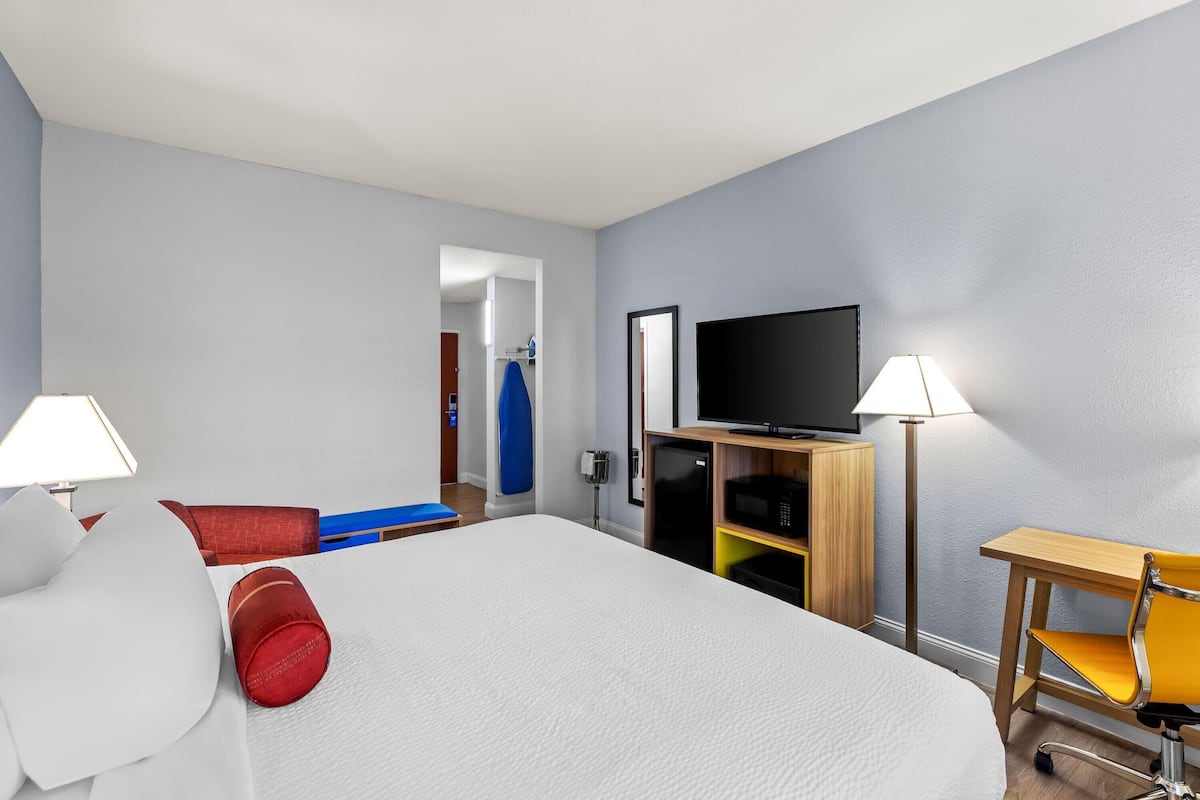 Una habitación de hotel con cama, escritorio, silla, televisor y lámpara.