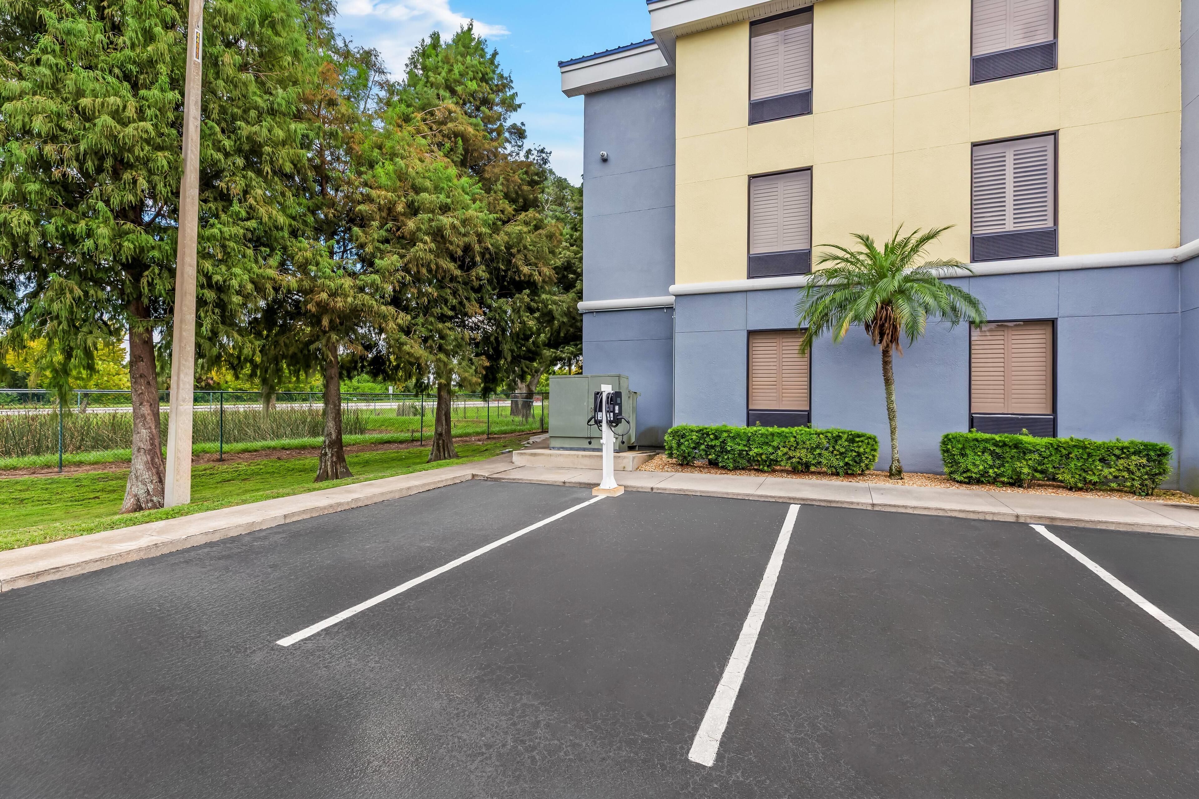 A parking lot with marked spaces, a building with multiple windows and shutters, and a palm tree.