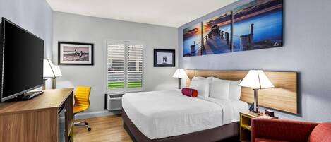 Une chambre d’hôtel avec un grand lit, un bureau avec une télévision, une chaise, un canapé rouge et des œuvres d’art accrochées aux murs.