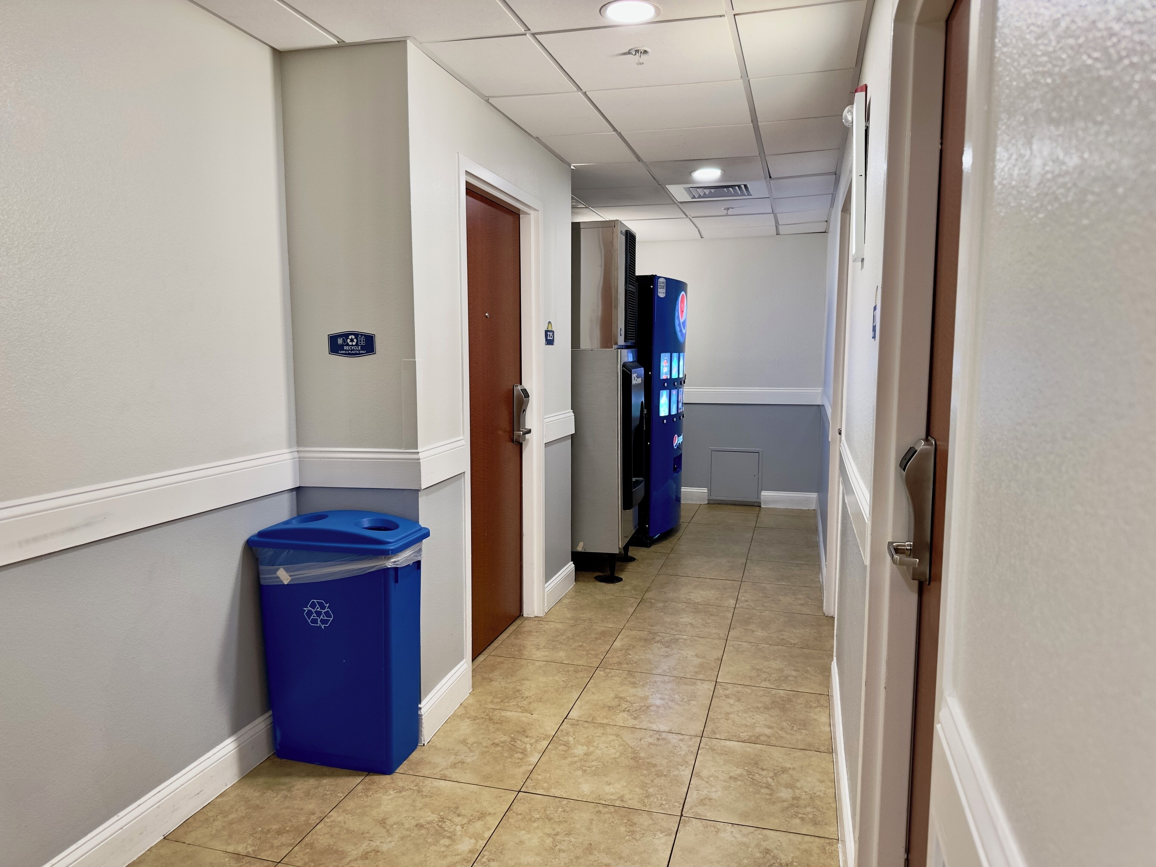 A hotel hallway with a blue recycling bin, a vending machine, and a door with a sign.