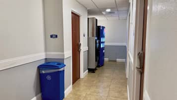 A hotel hallway with a blue recycling bin, a vending machine, and a door with a sign.
