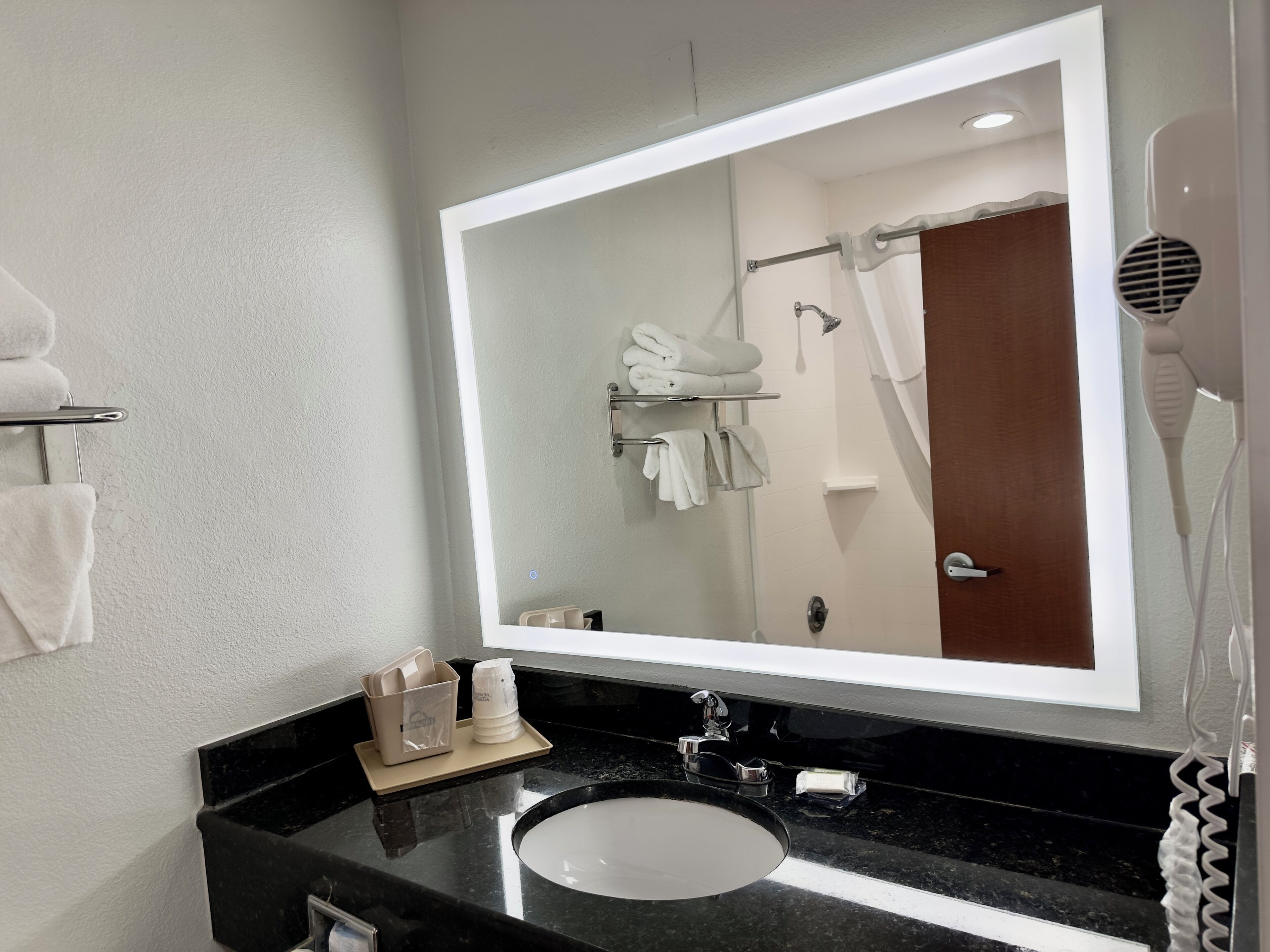 A bathroom with a large mirror, a sink, a towel rack, and a hairdryer.