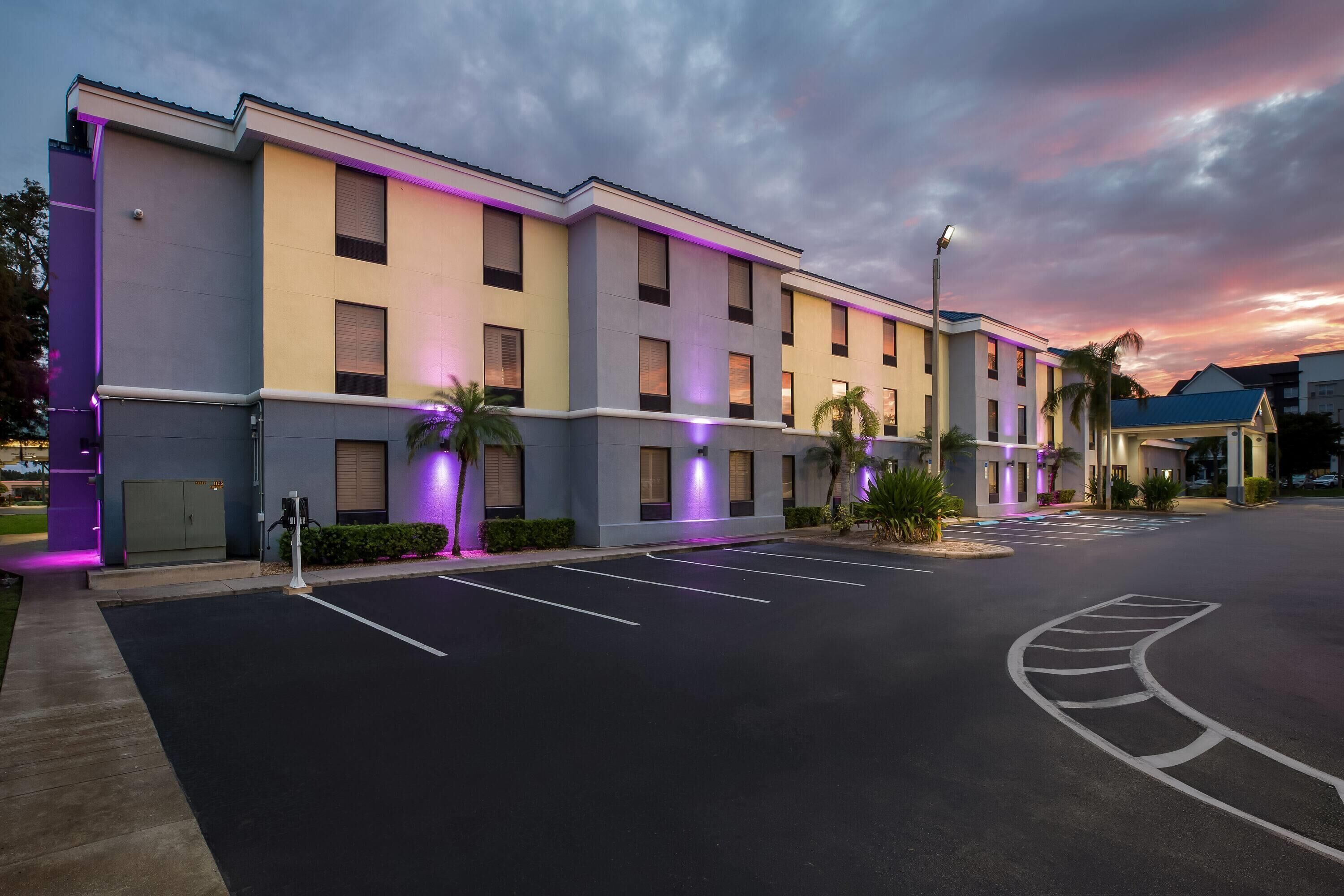 A modern hotel with a parking lot and a sunset sky.