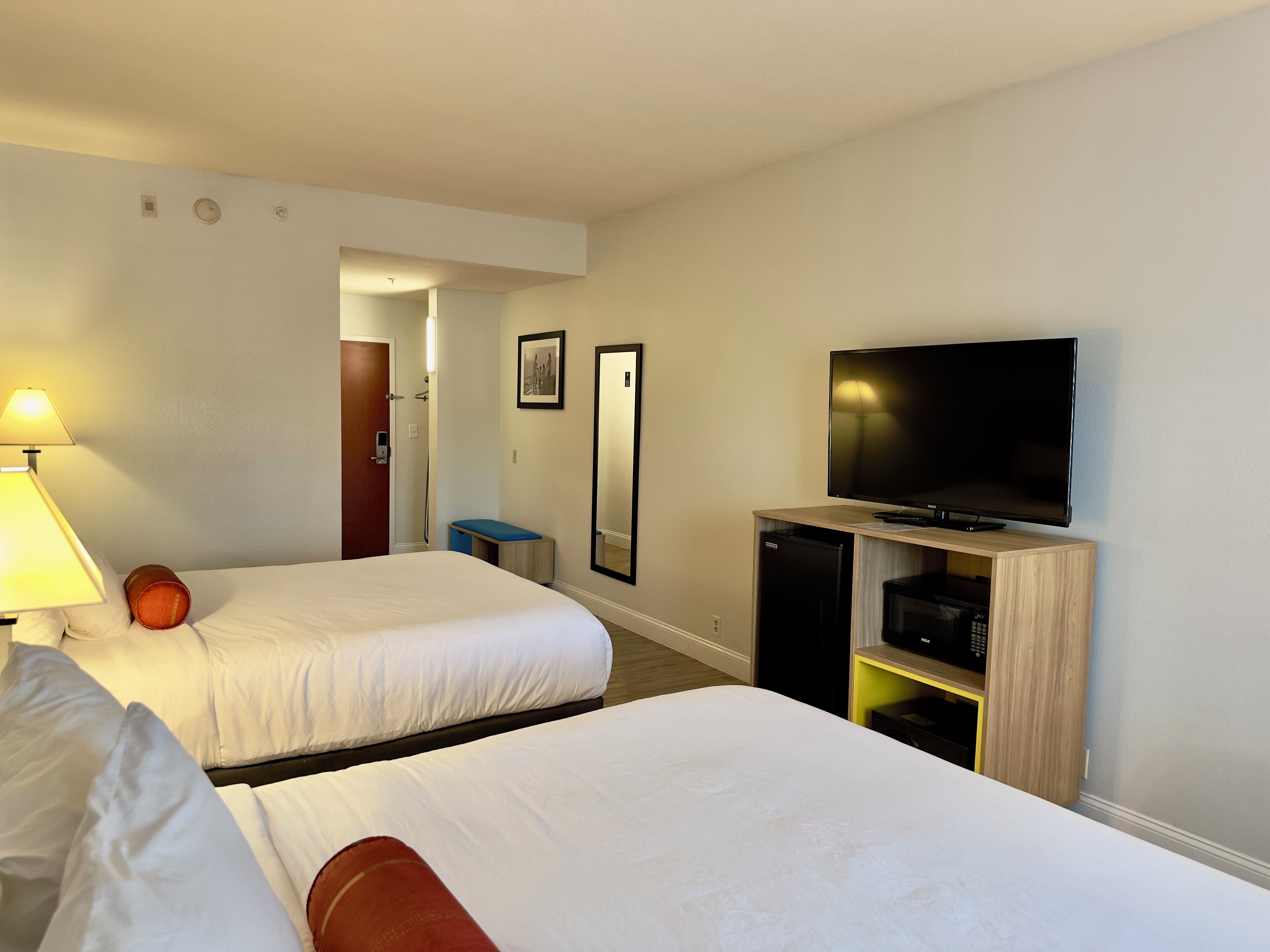 A hotel room with two beds, a TV, a desk, and a bathroom visible through an open door.