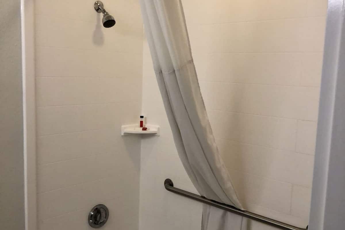 Ducha con puerta de vidrio, cabezal de ducha manual, grifo de mano y toallero.