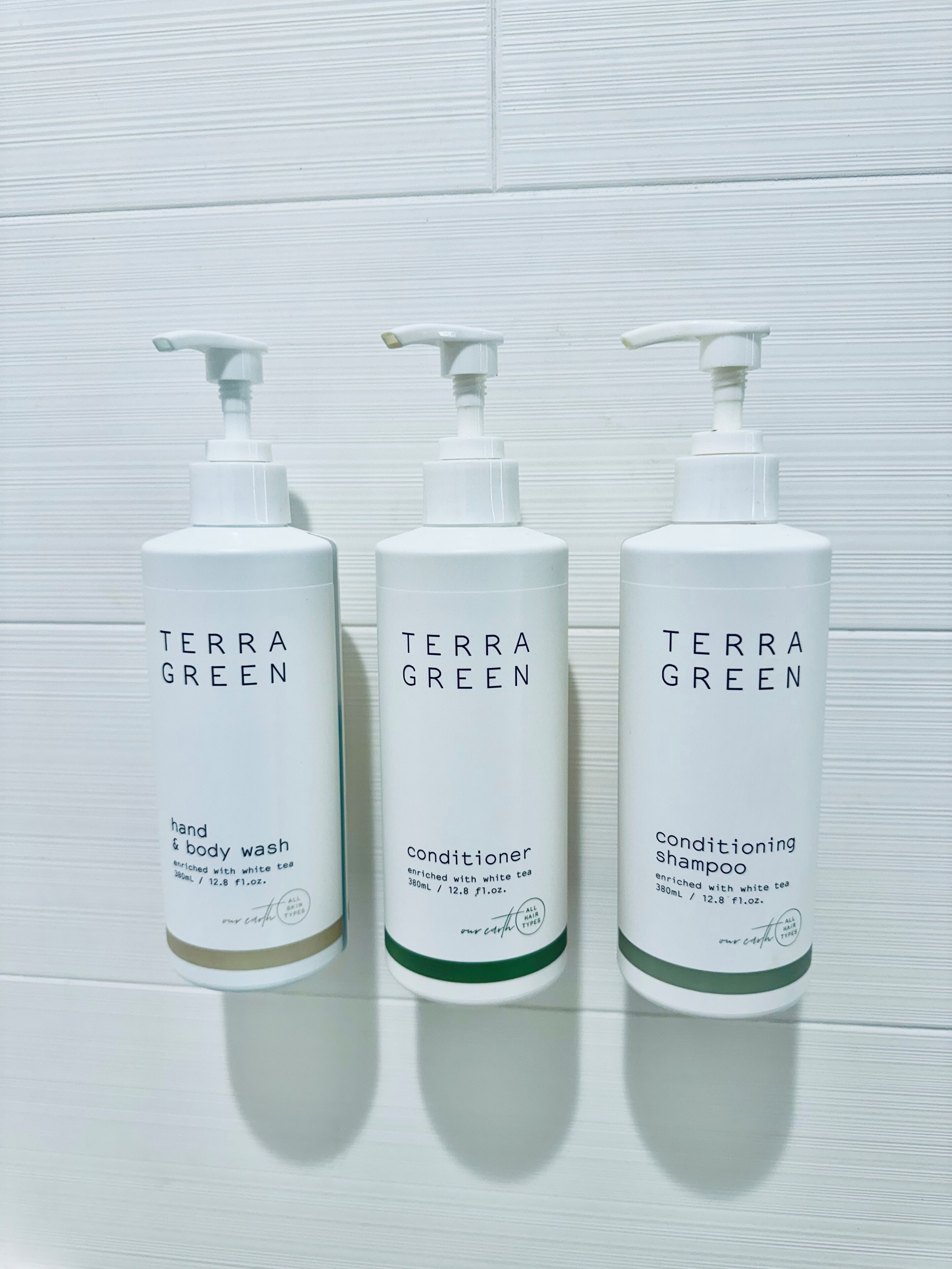 Three white Terra Green bottles against a white tiled wall.