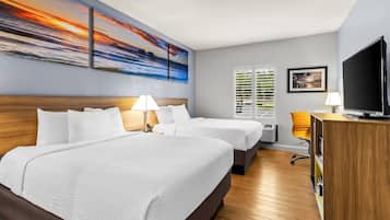 A hotel room with two beds, a TV, and a painting of a sunset.