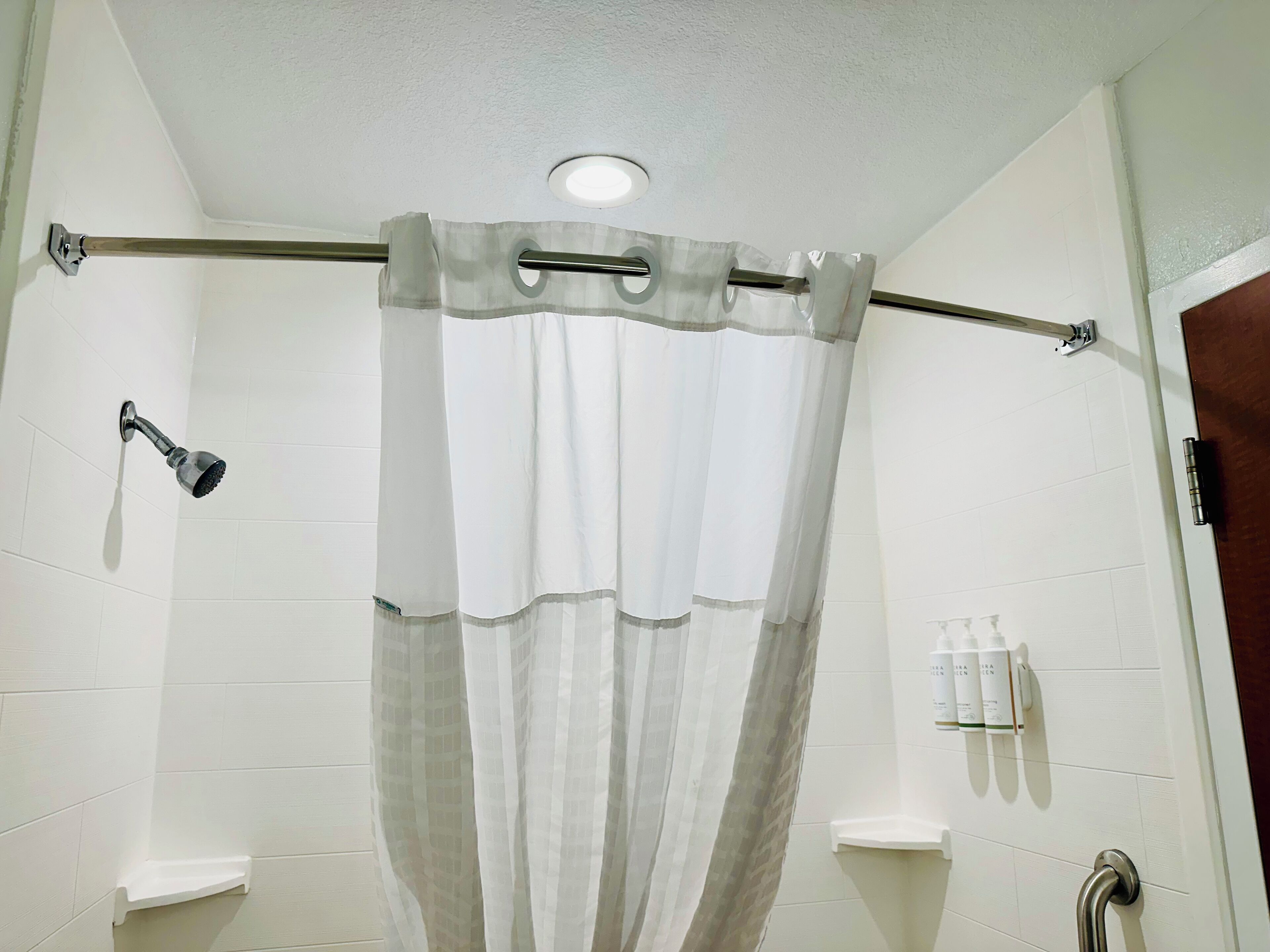 A shower with a curtain, a handheld showerhead, and a shelf with toiletries.