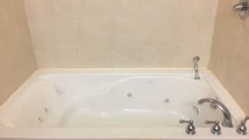 A rectangular bathtub with a single faucet and three separate controls, set against beige tiled walls.