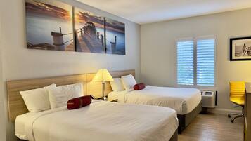 A hotel room with two beds, a nightstand, a lamp, a window with blinds, and a painting of a pier.