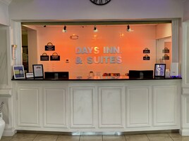 Un mostrador de recepción con un letrero que dice "Days Inn & Suites" y varios carteles informativos, incluyendo horarios de registro y servicios.