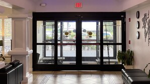 A hotel entrance with a glass door, an exit sign above, and a reception desk to the left.