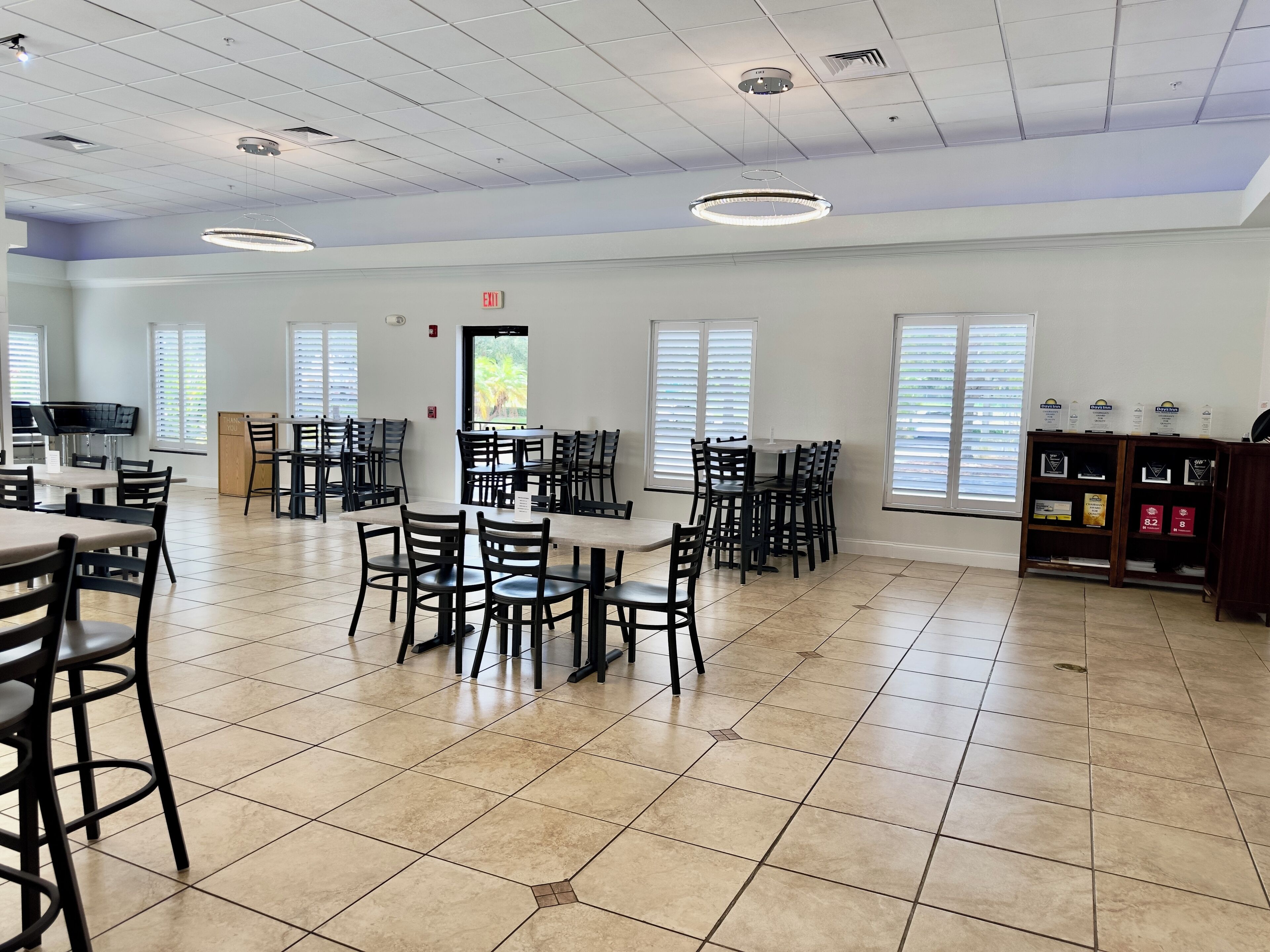 A spacious dining area with multiple tables and chairs, a kitchen area, and a view through the windows.