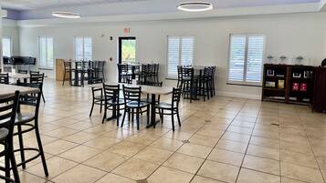A spacious dining area with multiple tables and chairs, a kitchen area, and a view through the windows.