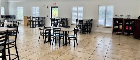 A spacious dining area with multiple tables and chairs, a kitchen area, and a view through the windows.