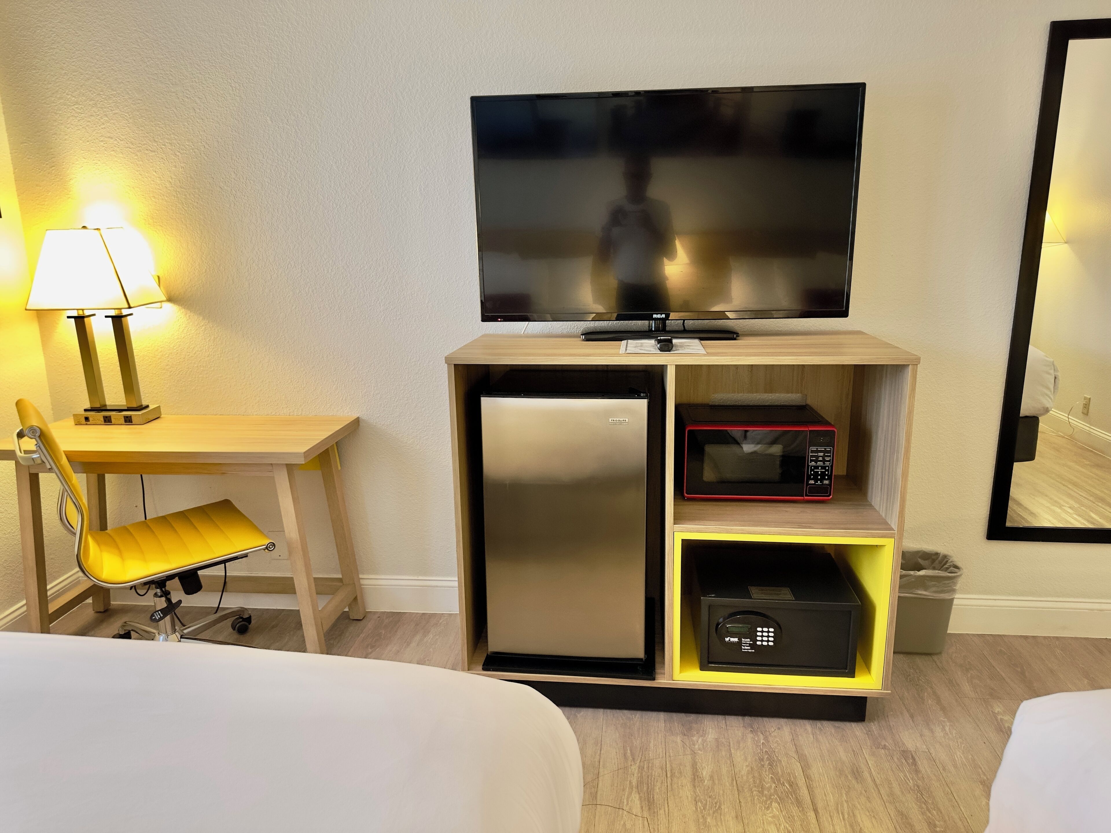 A hotel room with a bed, a desk with a lamp, a television, a microwave, and a mini-fridge.