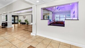 A spacious lobby with a tiled floor, a reception desk, and a seating area with chairs and a sofa.