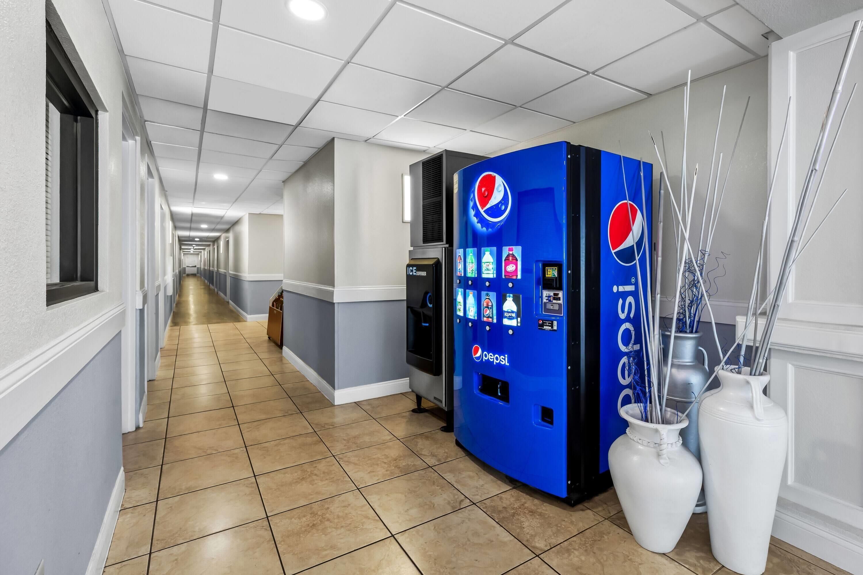 En hall med en försäljningsautomat för Pepsi, två vita vaser och ett kylskåp.
