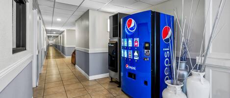 En hall med en försäljningsautomat för Pepsi, två vita vaser och ett kylskåp.