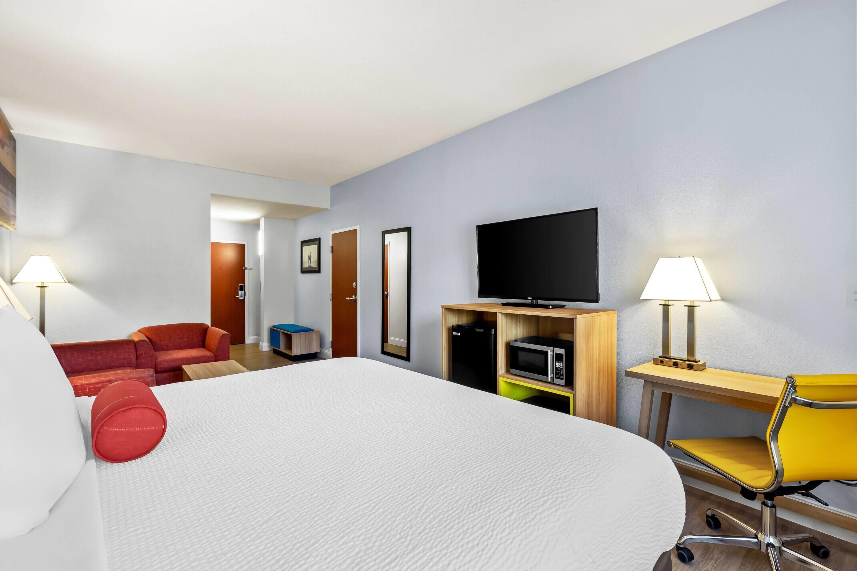 Una habitación de hotel con una cama grande, un escritorio con silla, televisor y microondas.