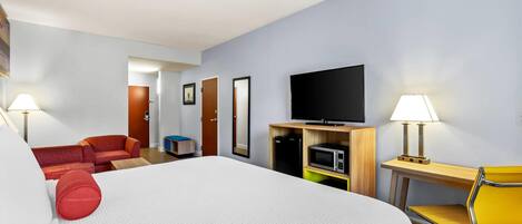 Una habitación de hotel con una cama grande, un escritorio con silla, televisor y microondas.