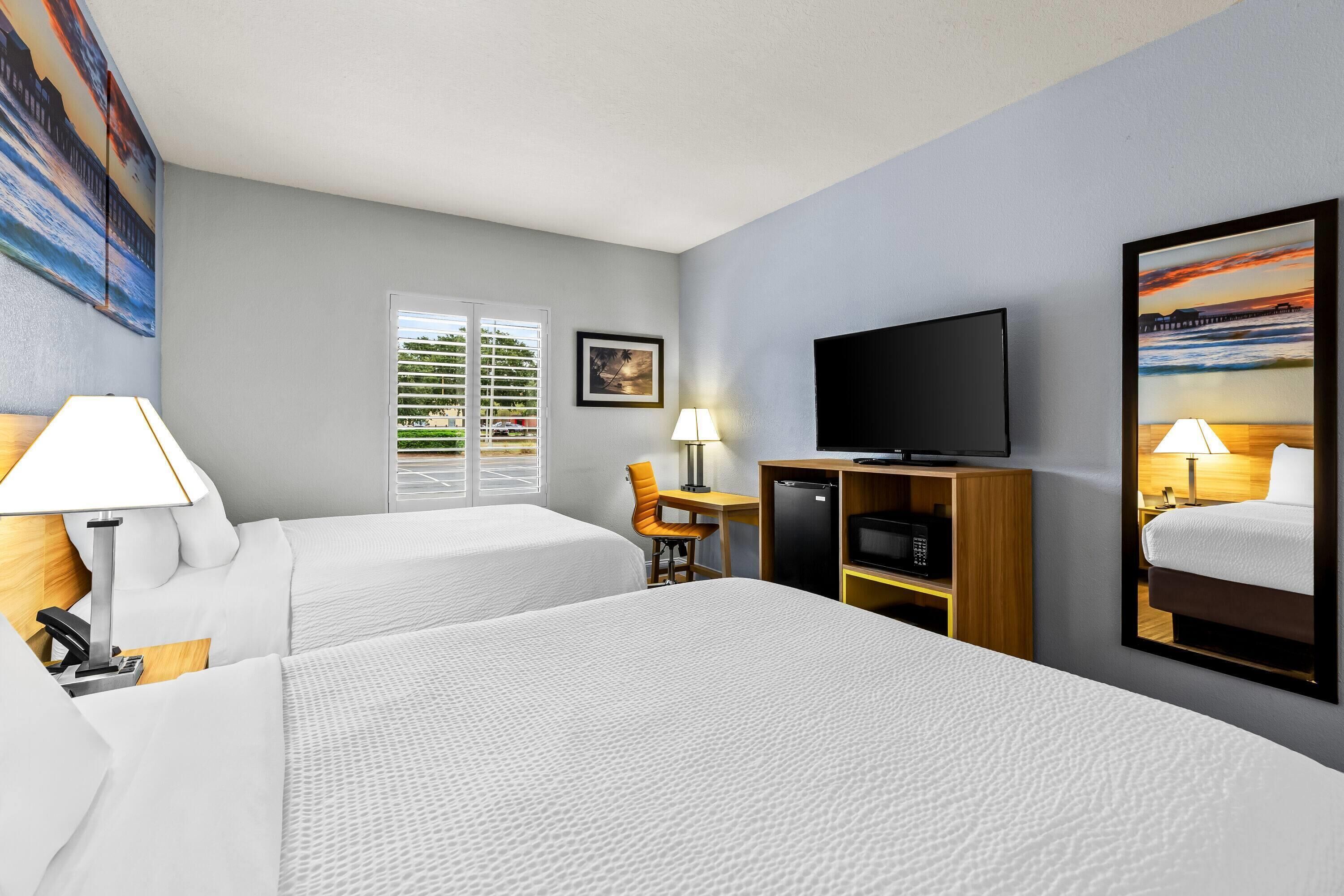 A hotel room with two beds, a desk, a television, and a window with blinds.