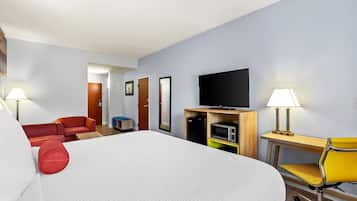 A hotel room with a bed, a desk with a chair, a television, a microwave, and a small seating area with a red couch and a yellow chair.