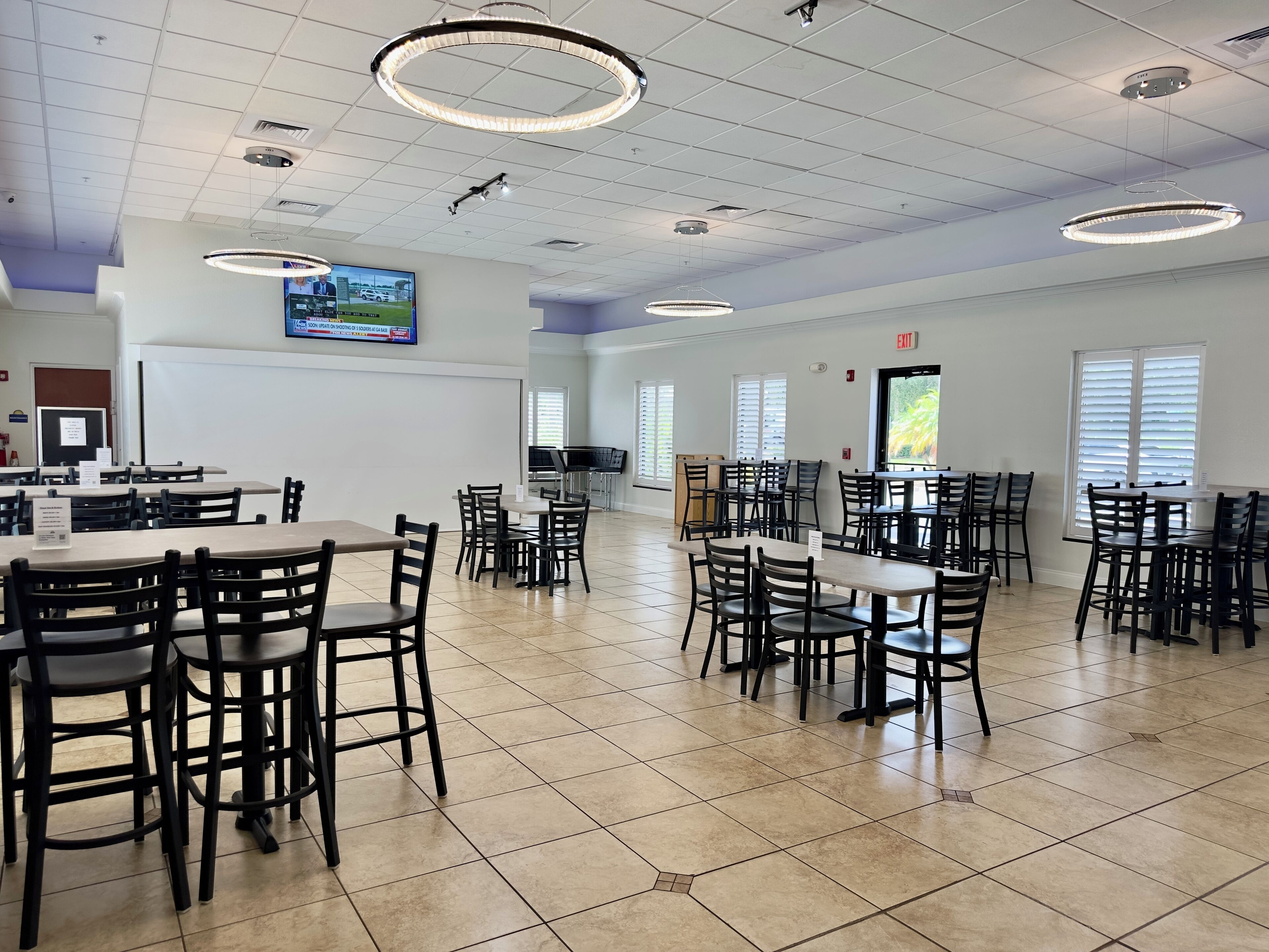 A spacious dining area with multiple tables and chairs, ceiling lights, and a television screen.