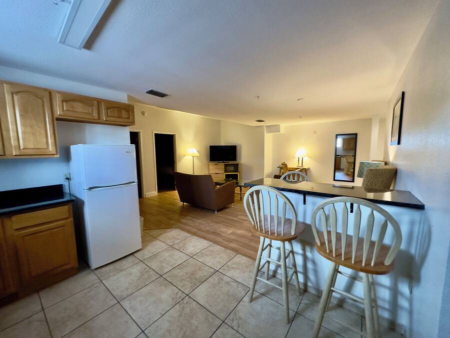 A compact kitchen with a refrigerator, wooden cabinets, and a dining area with two chairs and a table.