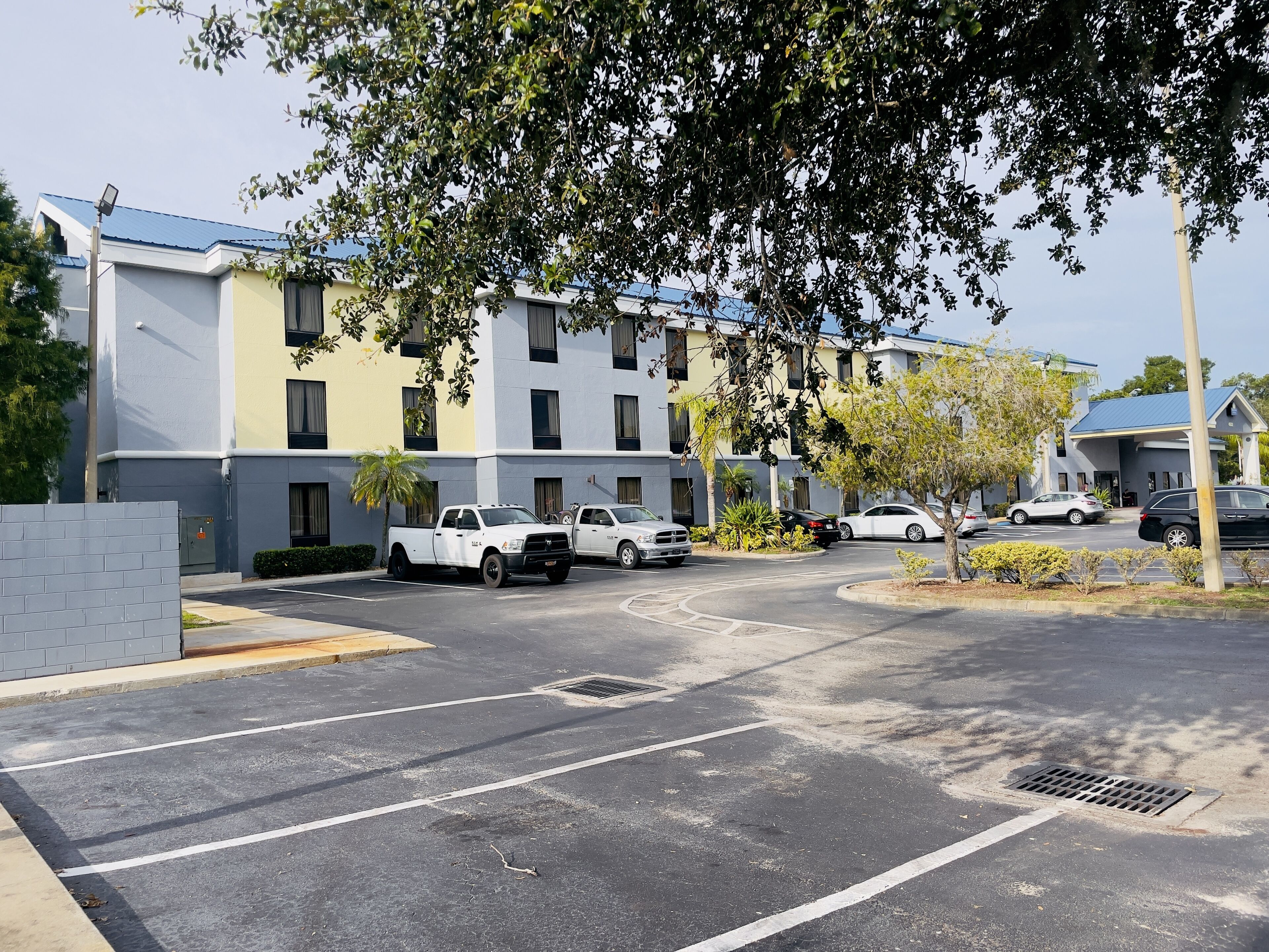 A parking lot with several vehicles, including a white pickup truck and a black SUV, in front of a multi-story building with a blue roof.