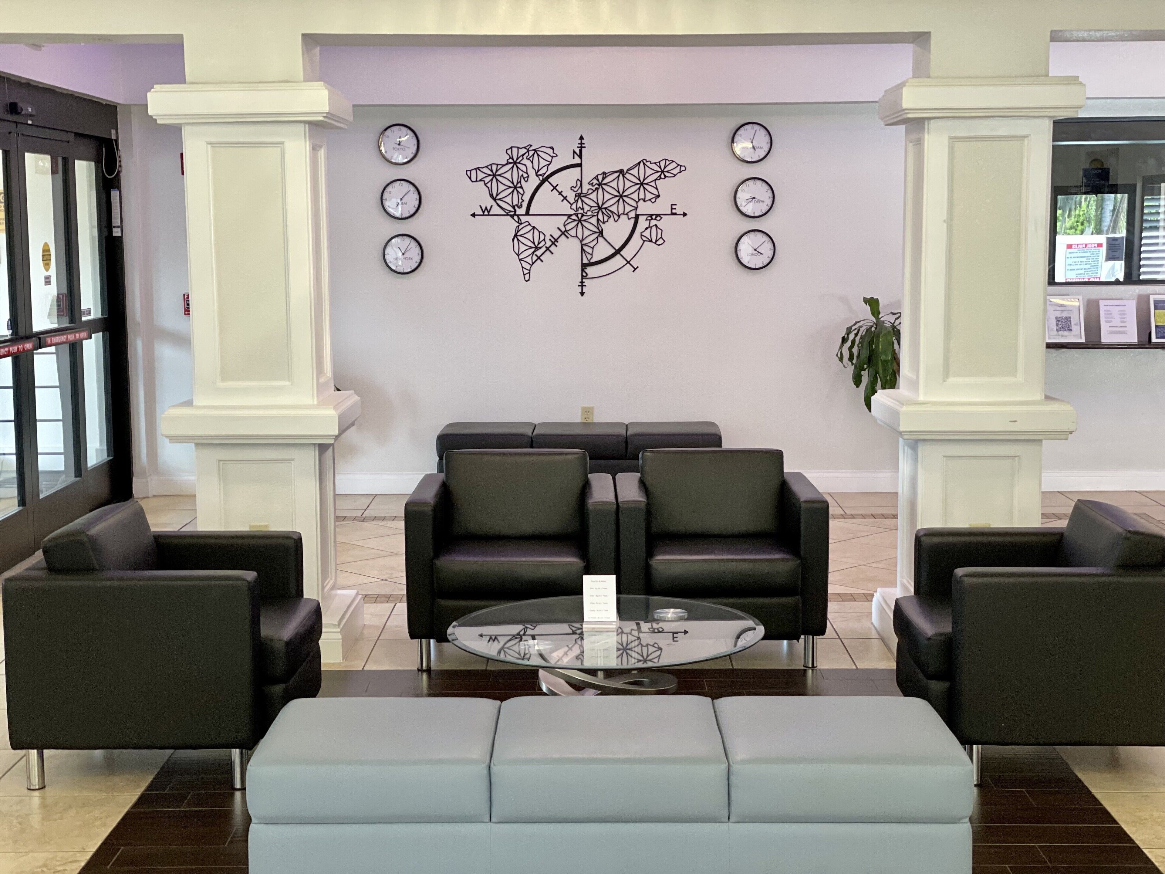 Un hall con mostrador de recepción, dos sofás de cuero negro, una mesa de centro de vidrio y una pared decorada con relojes y una obra de arte geométrica.