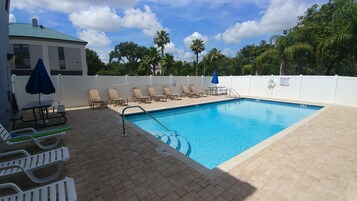 Una piscina con sillones de descanso y una mesa de picnic, rodeada por una valla blanca y palmeras.