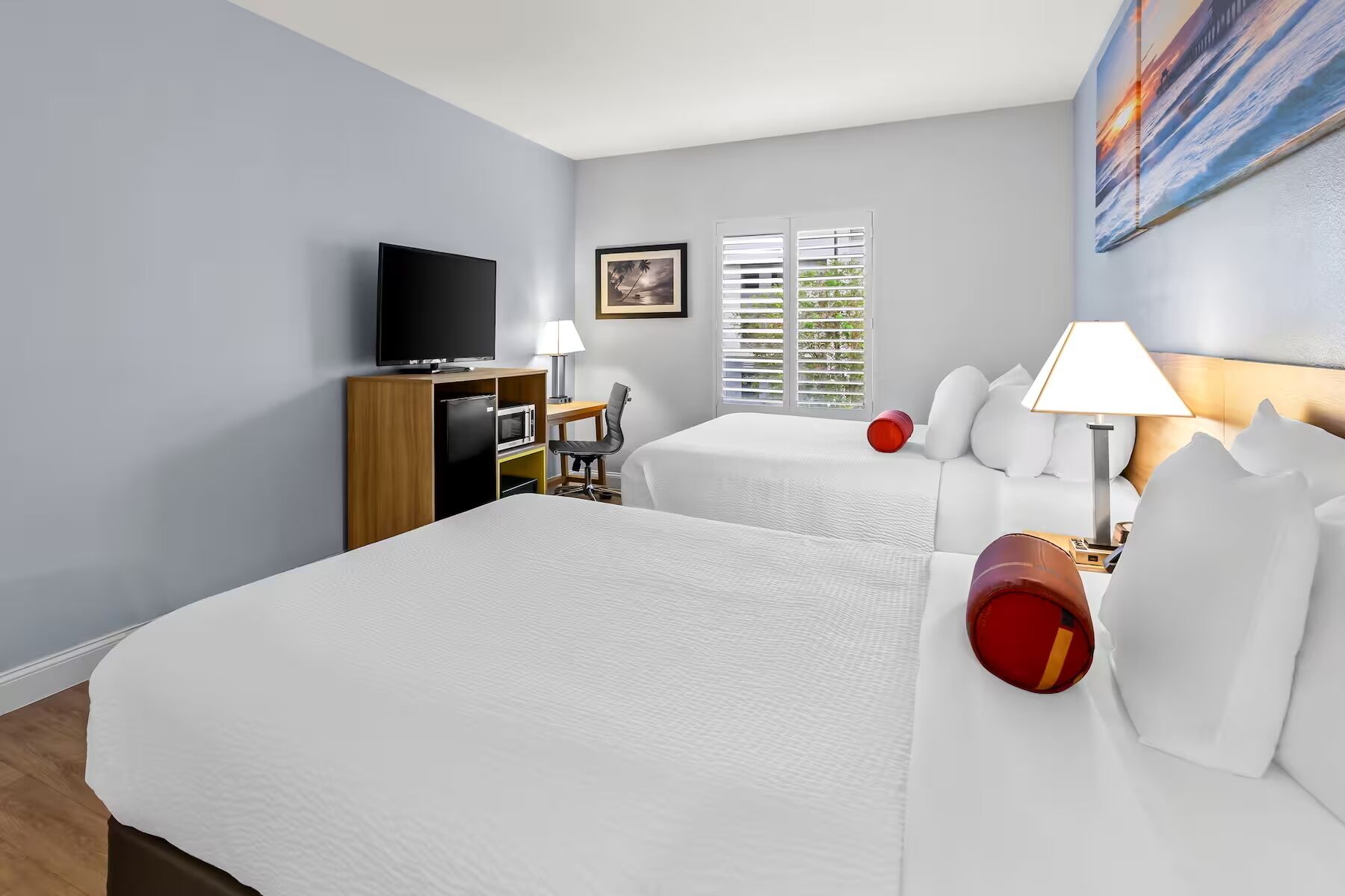 A hotel room with a large bed, a TV, a desk, and a window with blinds.