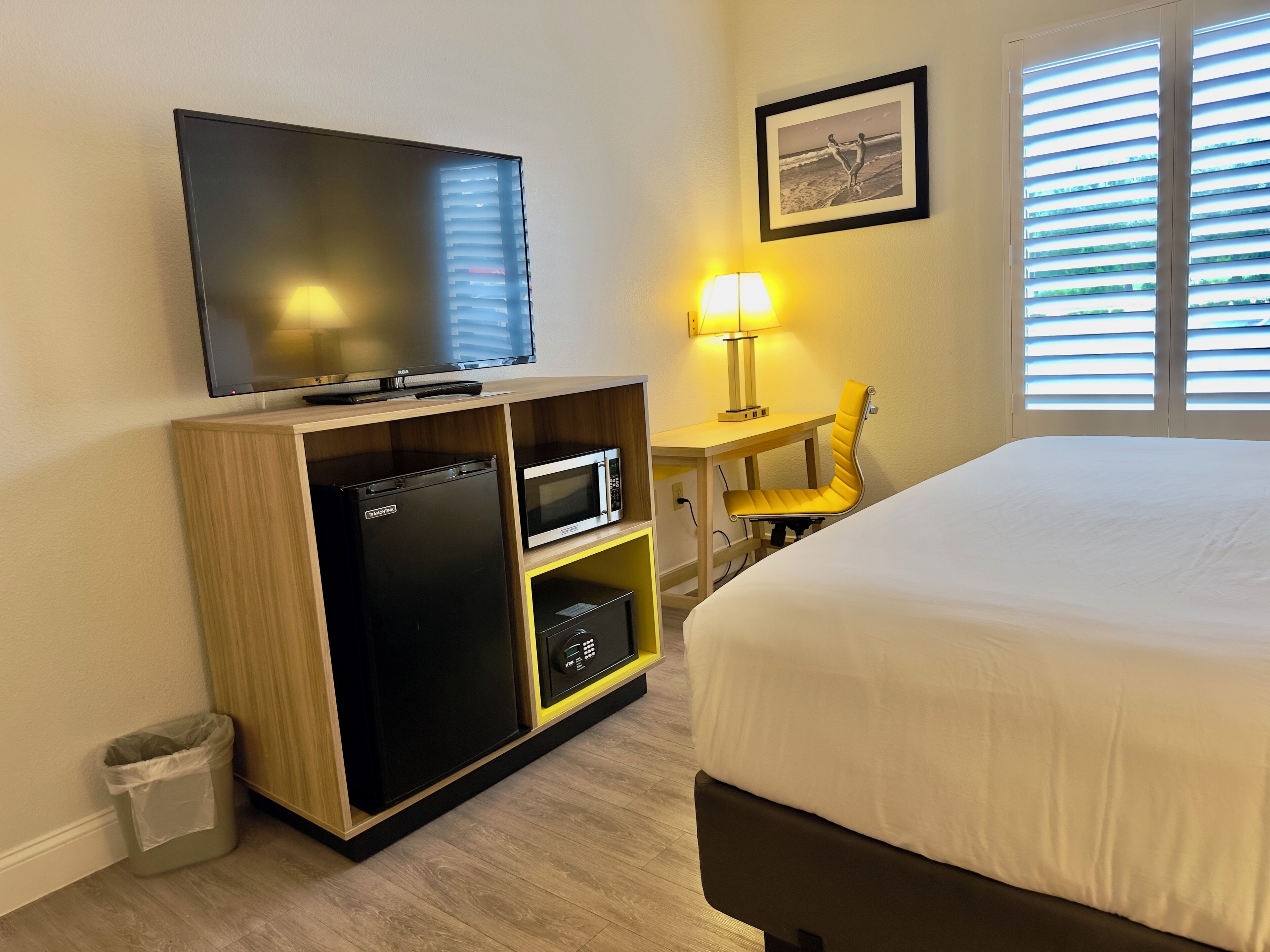 Ein Hotelzimmer mit Bett, Fernseher, Mikrowelle, einem kleinen Schreibtisch mit Lampe und einem Sessel.