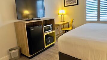 Ein Hotelzimmer mit Bett, Fernseher, Mikrowelle, einem kleinen Schreibtisch mit Lampe und einem Sessel.