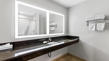 A modern bathroom with a large mirror, black granite countertop, white sink, and a towel rack with folded towels.