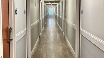 A long, narrow hotel corridor with doors on both sides, a wooden floor, and a ceiling with recessed lighting.