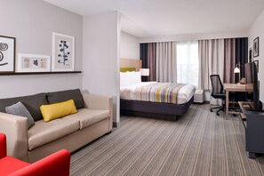 A hotel room with a bed, a desk, a chair, a sofa, and a red armchair.