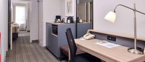Habitación de hotel con escritorio, silla, teléfono y espejo.