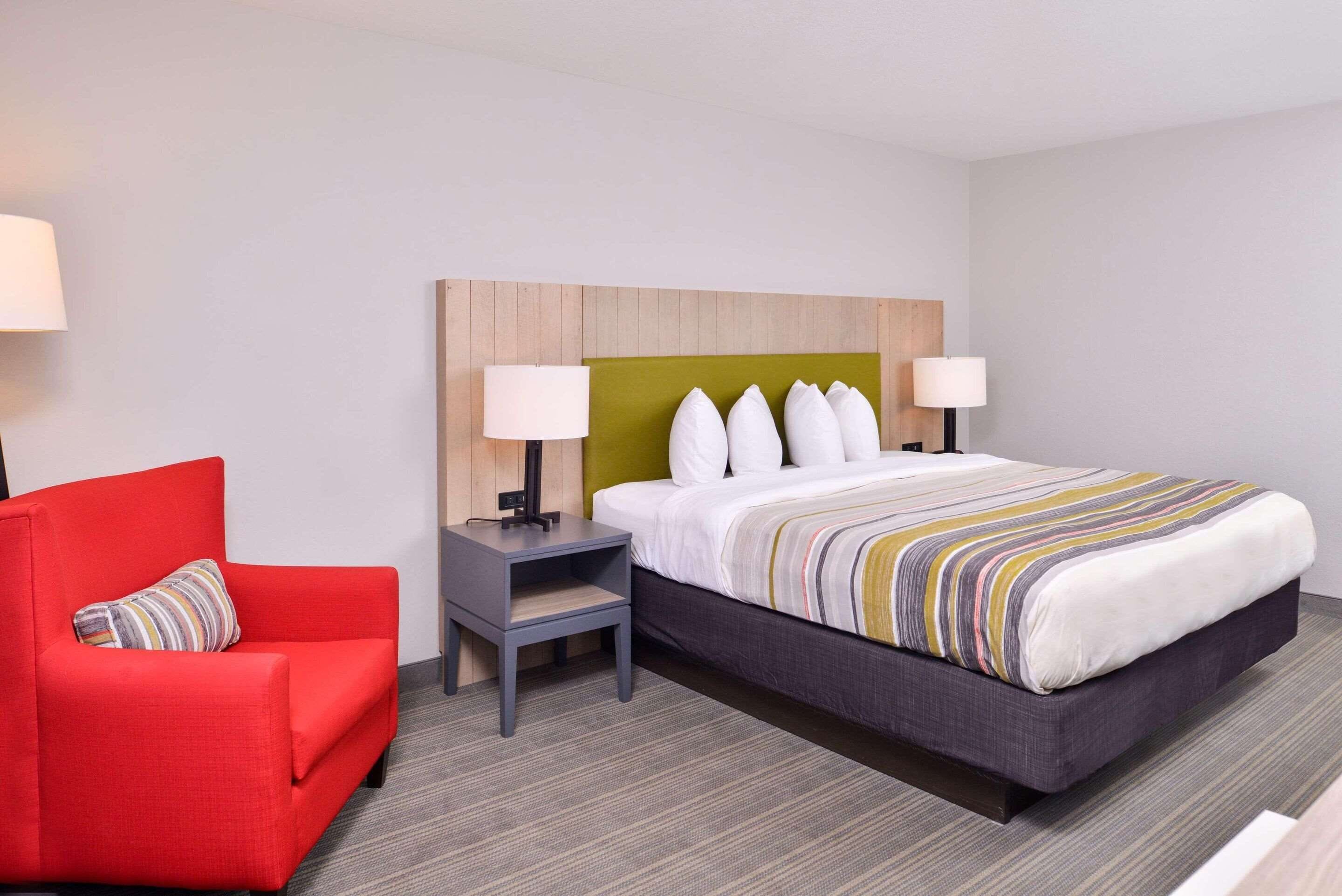 Une chambre d’hôtel avec un lit, un fauteuil rouge, une table de chevet et deux lampes de chevet.