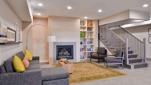 Ein modernes Wohnzimmer mit grauem Sofa, Kamin, Bücherregal und Treppe.
