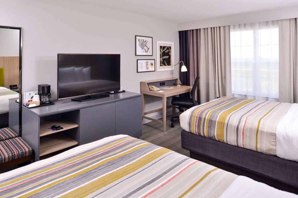 Une chambre d’hôtel avec un lit, un bureau équipé d’un ordinateur, une télévision et une fenêtre avec des rideaux.