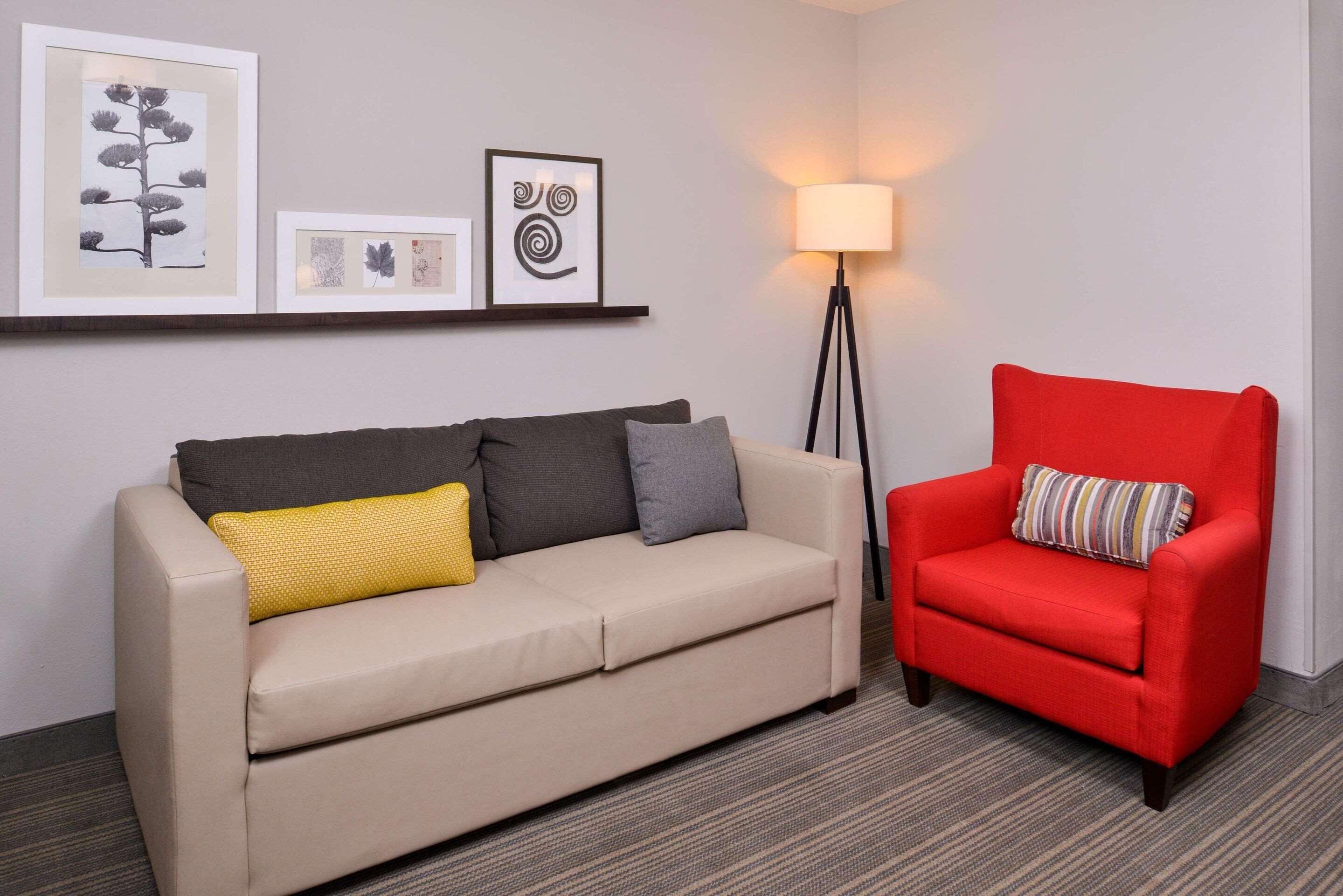 A room with a beige sofa, a red armchair, and a floor lamp.