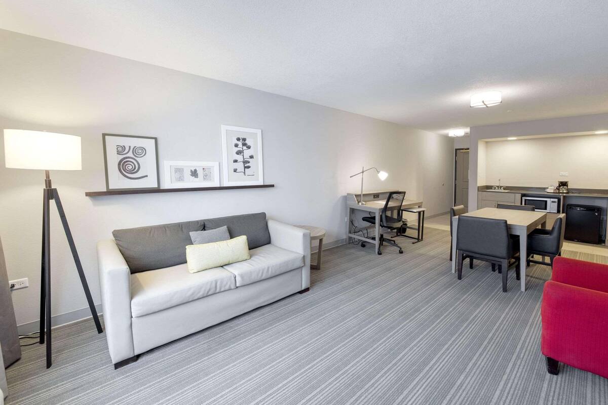 Une chambre d’hôtel moderne avec un canapé blanc, une table à manger avec des chaises, un bureau avec une chaise et un coin cuisine.