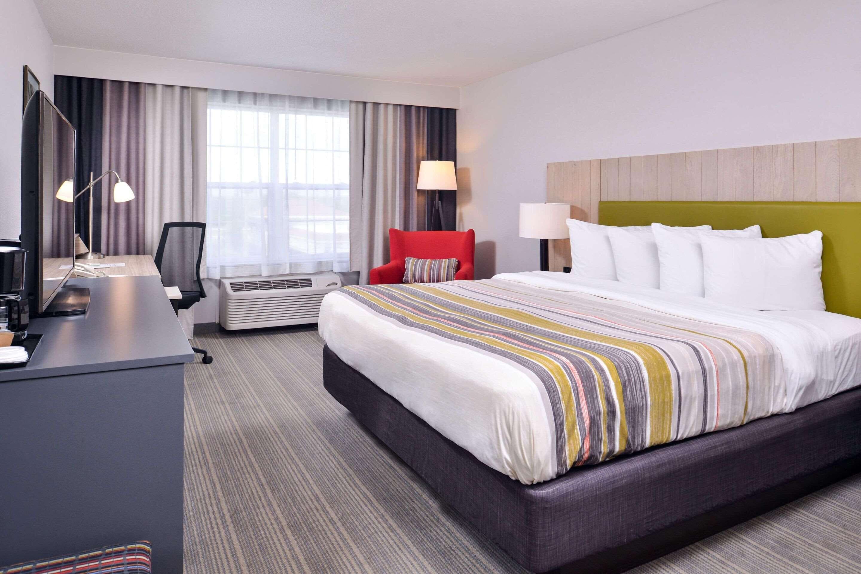 Une chambre d’hôtel avec un grand lit, un bureau avec un ordinateur, une chaise et une fenêtre avec des rideaux.