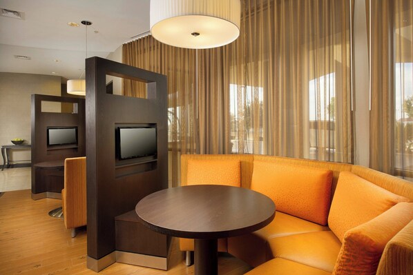 Una habitación de hotel moderna con una mesa redonda, sofá naranja y un televisor montado en una partición de madera.