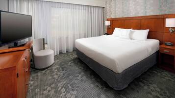 A hotel room with a large bed, a television, a desk with a chair, and a nightstand with a lamp.