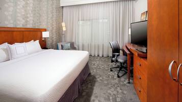 A hotel room with a large bed, a desk with a chair, a television, and a wardrobe.